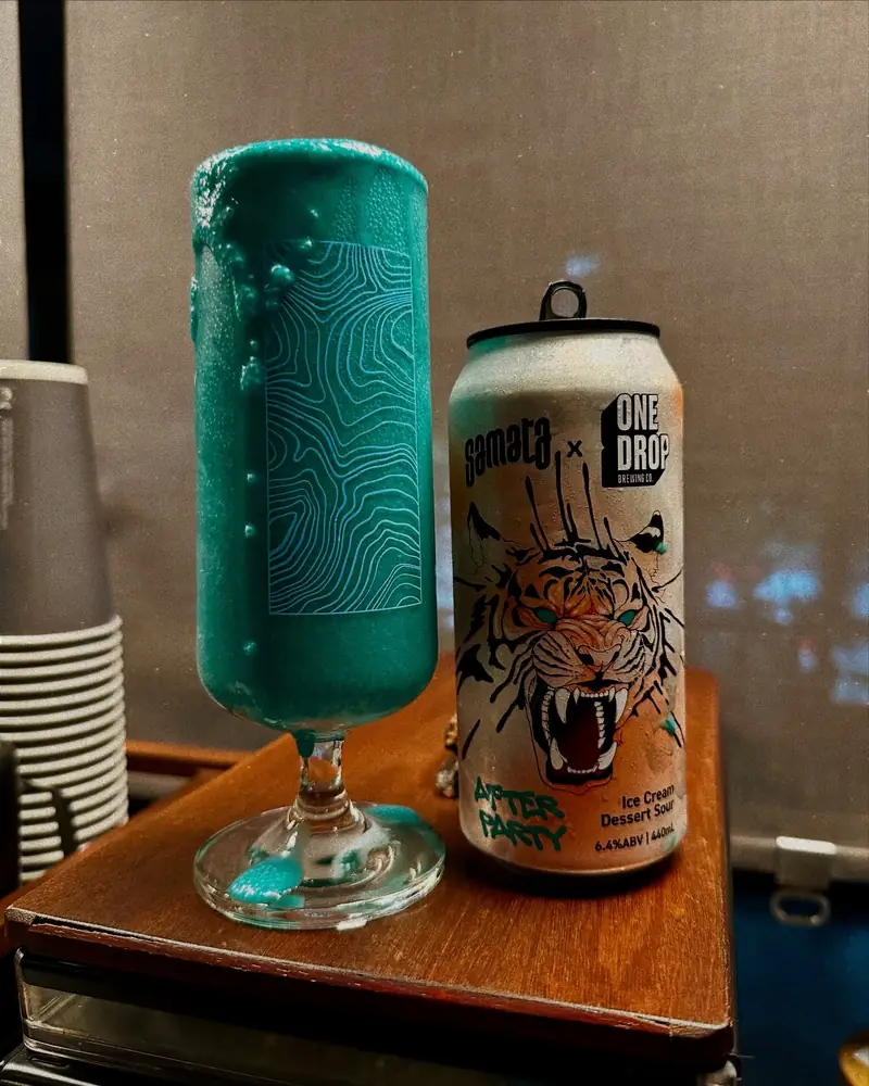 Teal embossed glass beside a tiger-label can at the taproom